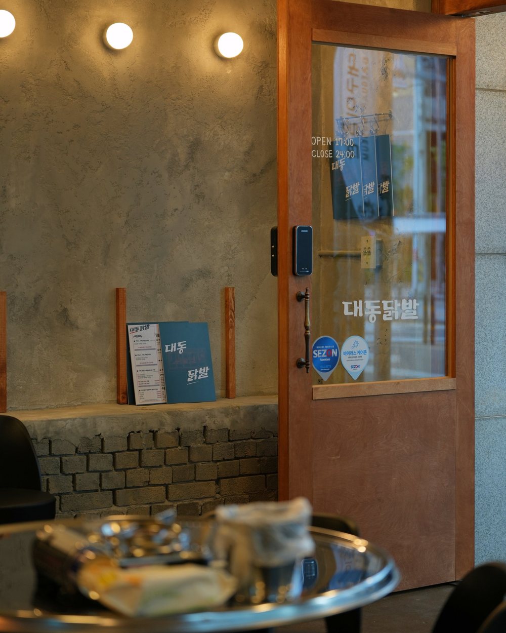 유럽미장 · 둥근 벽등 아래 회색 유럽미장 벽과 나무 문, 대구 칠성동 닭발집