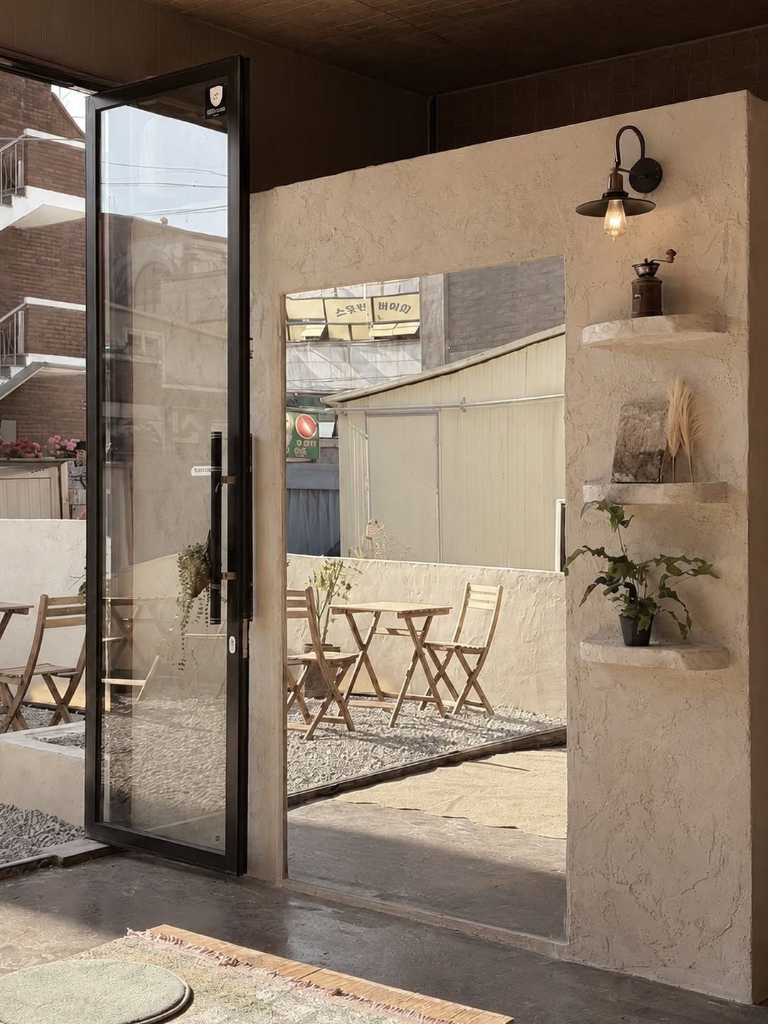 인천 HUS 카페. 유럽미장 벽에 낸 선반과 벽등, 유리문 너머 바깥 자리